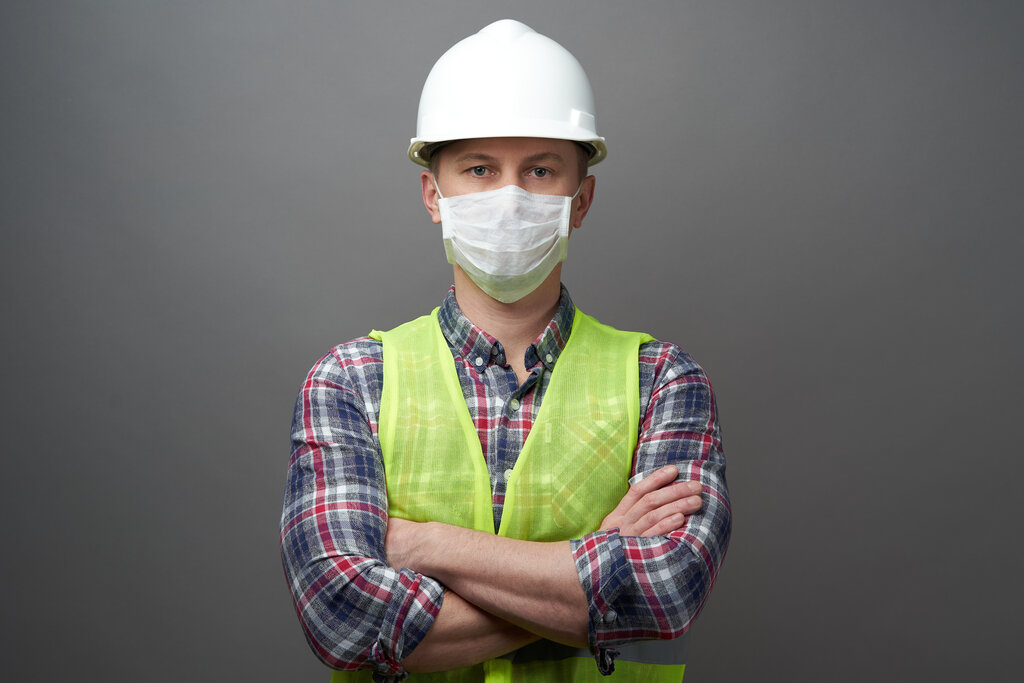 Worker man wearing hygienic mask and protective hard hat. Young engineer worker wear a white helmet and medical face mask. Coronavirus Hygiene, safety concept