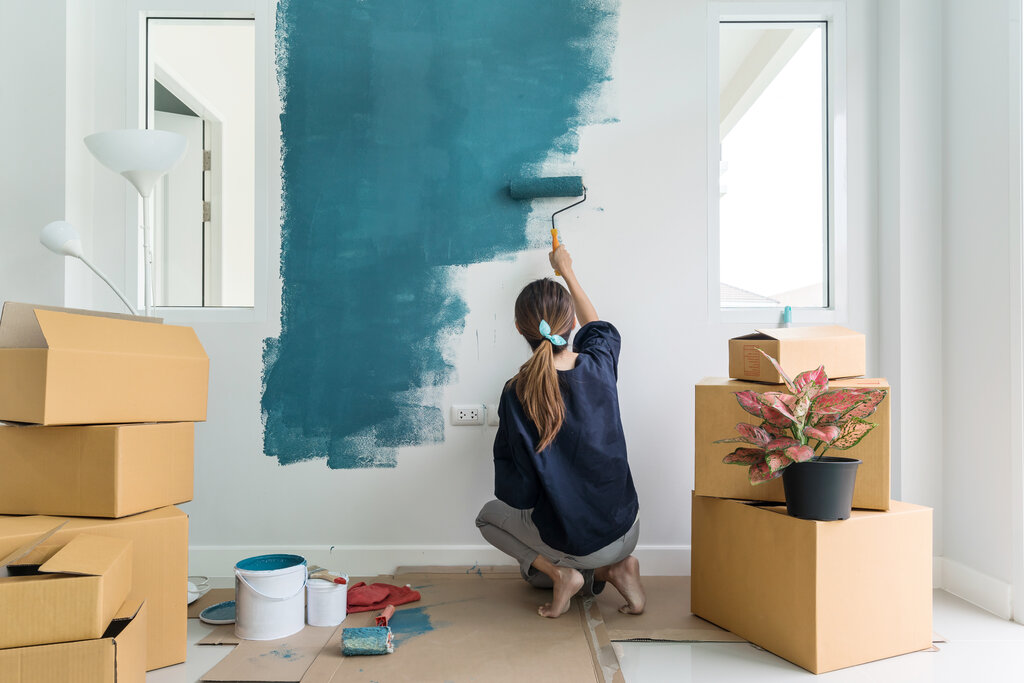 Young happy woman painting interior wall with paint roller in new house