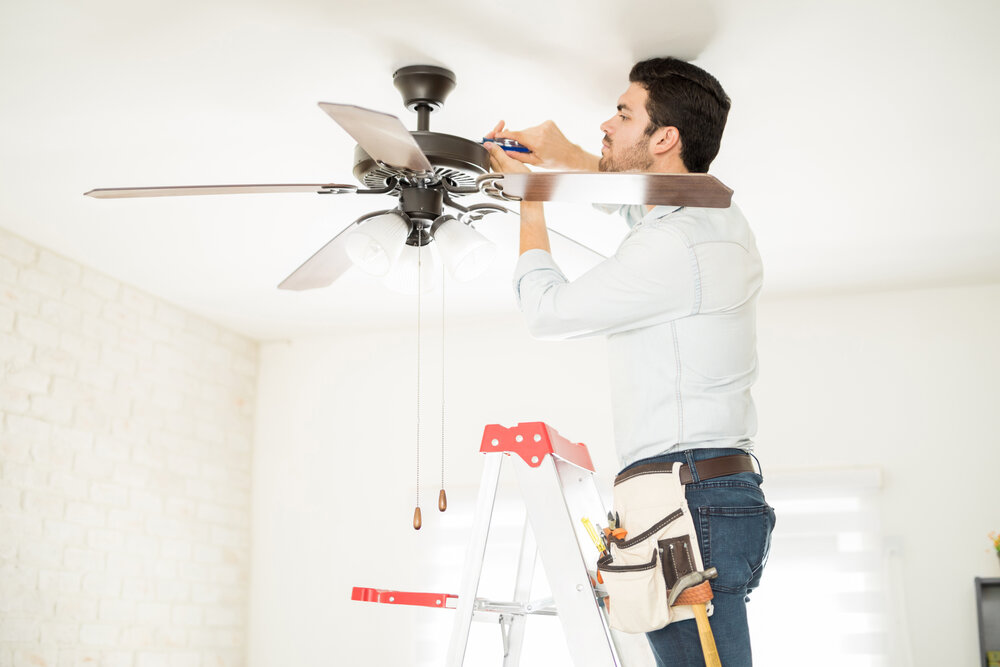 Technician on a ladder installing a ceiling fan