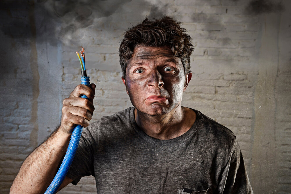 young man holding electrical cable smoking after domestic accident with dirty burnt face in funny sad expression in electricity DIY repairs danger concept in black smoke background
