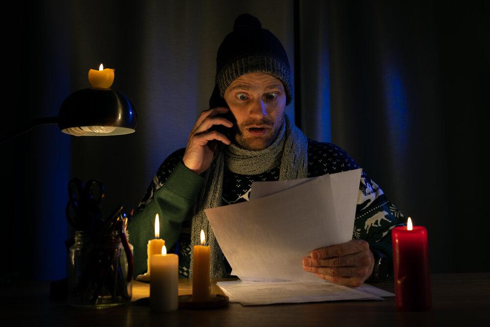 shocked man in candle light looking at high bills for electricity, gas heating in cold dark room at home. energy crisis and inflation concept