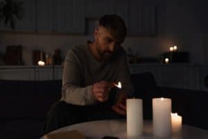 man holding burning match while lighting candles in dark kitchen during power outage,stock image