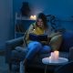 Young woman reading book with flashlight at home during blackout. She lacks a generator transfer switch to keep power running during outage