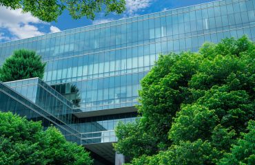 Eco-friendly building in the modern city. Sustainable glass office building with trees for reducing heat and carbon dioxide. Office building with green environment. Smart technology concept.