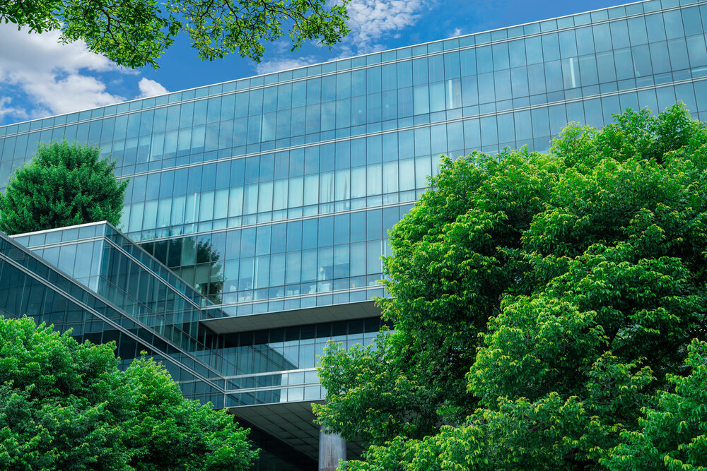 Eco-friendly building in the modern city. Sustainable glass office building with trees for reducing heat and carbon dioxide. Office building with green environment. Smart technology concept.