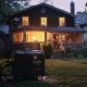 Gasoline generator providing electricity to a suburban house during a nighttime power outage. the scene shows a lit up home with a family comfortably inside, the practical use of the generator amidst dark surroundings.