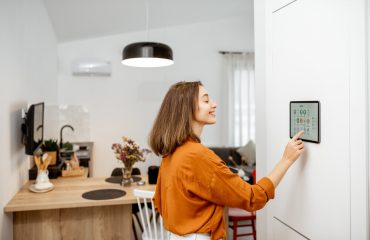 Young woman controlling home with a digital touch screen panel installed on the wall in the living room. Concept of a smart home and mobile application for managing smart devices at home. Example of 2025 remodeling trends