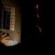 A man, visible only as a faint silhouette, is using a flashlight to investigate a home fuse box in his basement during a power outage. Circuit breaker trips when it rains.