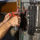 Electrician working on a circuit breaker panel is installing a ground wire using a power drill. Selective focus