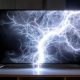 A flat screen television shows a graphic of lightning striking. The image is dark and moody, with white lightning bolts on a black background. The television is positioned on a white wooden entertainment center in a dimly lit room.