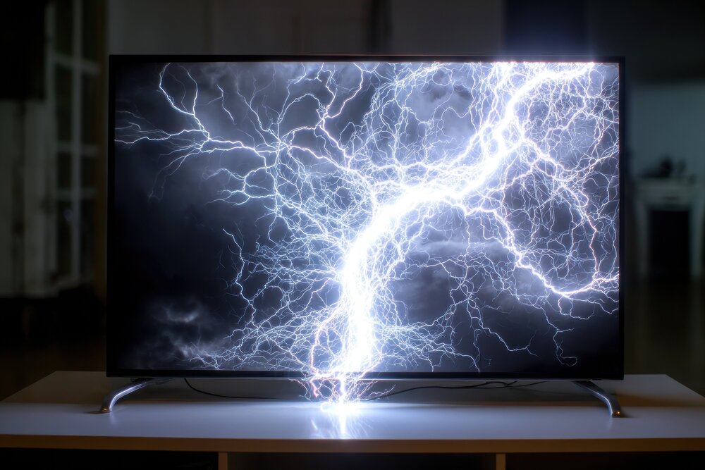A flat screen television shows a graphic of lightning striking. The image is dark and moody, with white lightning bolts on a black background. The television is positioned on a white wooden entertainment center in a dimly lit room.