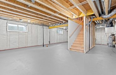 Large, empty basement with a staircase leading up to the second floor. The walls are white and the floor is gray
