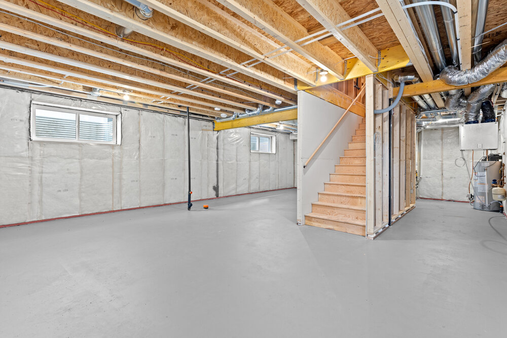 Large, empty basement with a staircase leading up to the second floor. The walls are white and the floor is gray