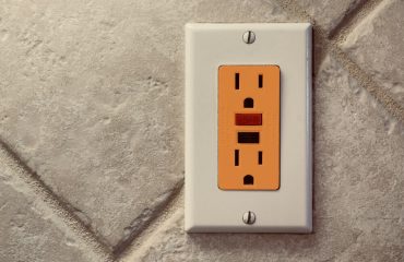 orange electrical outlet against a tiled wall