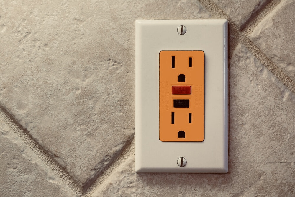 orange electrical outlet against a tiled wall