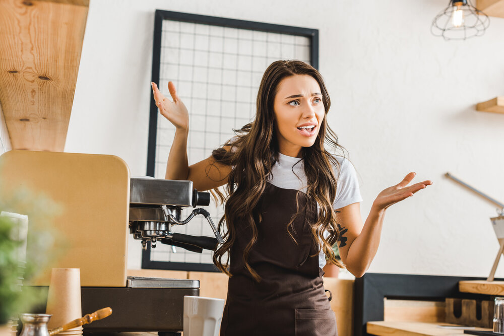 angry barista in brown apron standing near coffee machine in coffee house, appliance won't work